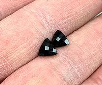Pair of black trillion checkerboard cut onyx gemstones shown on fingertip for scale