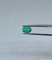 Emerald held in tweezers, side view showing oval shape and green colour