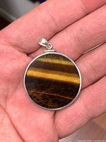 Front view of round tiger's eye pendant in hand