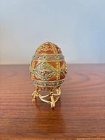 Front view of orange enamel jeweled egg on gold-tone stand showing lattice and rhinestone detailing