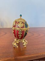 Closed Joan Rivers red and green enamel egg on gold mythical creature stand