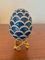 Front view of blue enamel egg on gold-tone stand, showing scallop rhinestone pattern