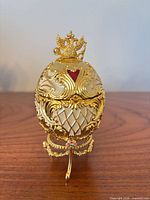 Closed egg front view showing crown finial, scrollwork, heart cartouche, stand