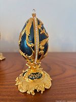 Closed blue enamel egg on pedestal base marked 2000 with gold scrolls and rhinestone band