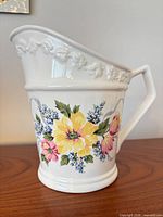 Profile view of porcelain pitcher vase showing floral design, handle, raised vine rim