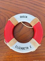 Front view of red and white souvenir lifebuoy marked Queen Elizabeth 2