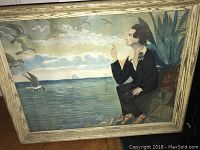 Watercolor painting showing a side profile of a person in dark clothing sitting by water with birds flying near and sailboat on horizon, in a wooden frame.