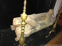 Close-up view of one brass andiron with electric log set behind it inside fireplace insert.
