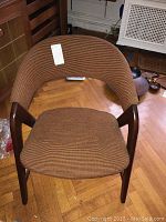 Front view of the teak Mid-Century Modern Danish armchair showing the curved backrest, armrests, and spring-loaded seat cushion upholstered in brown patterned fabric.