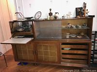 Full view of Mid-Century Modern buffet dry bar showing wood finish, glass front upper shelves, and sliding wooden lower doors with caned panels.