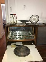 Photo showing silverplate lidded bowl with tarnished surface, two wine bottle holders, and multiple platters including glass and marble trivet on wood furniture.
