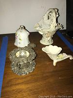 Overview photo showing the silver plated tea strainer and holder, small white porcelain bell with floral accents, basket-shaped porcelain vase, and small floral porcelain dish.