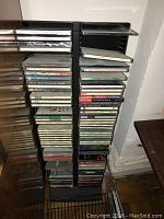 Black plastic CD rack holding a stacked collection of CDs, viewed from front and partially side.