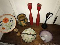 Top view of all the items on surface showing silver plated bud vase, ceramic basket, red candlesticks, black vase, plate and small figurine.
