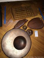 Group photo of all wooden serving ware items showing large round footed platter, small stemmed dish, two small bowls, two small shaped plates, and rectangular pierced wooden tray on wooden floor.