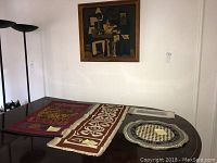 Wide view showing vintage framed abstract print hanging on wall and three assorted textiles laid out on table, including one rectangular and two round pieces with varied designs.