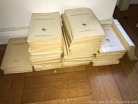 Stack of 28 softcover books with beige covers and Russian text stacked on wooden floor.