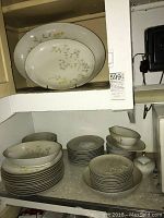 Full set displayed on shelves showing multiple stacks of plates, bowls, platters, gravy boat and creamer with Alicia pattern in soft floral and gold accents.