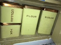 Four vintage metal tins labeled Coffee, Tea, Flour, and Sugar with copper lids, showing minor wear and patina.