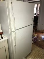 Front and right side view of the white General Electric refrigerator showing vertical handles and some exterior wear.