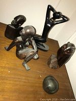 Four black sculptures displayed on a wooden surface: three women and one animal figure, the latter not included in sale per owner.