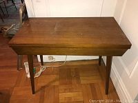 Front view of Mid Century Modern wooden folding table, showing flat top and tapered legs on parquet floor.