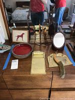 Photo of table surface showing Australian wood decor including framed fabric art pieces, wooden boomerang, vintage brass desk pad, red ceramic bowl, vintage dustpan with brush, red tray, wooden bookends and an oval mirror on stand.