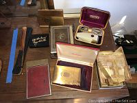 Photo showing various vintage items including lighter in fancy box, Schick electric razor in original case, toiletry kit in original box, note pad, cigarette cases, carved wooden handled item and a small black box.