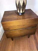 Top and front view of one night table showing two drawers and wood grain finish with table lamp on top