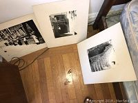Three framed and matted black and white photographs leaning against a wall on a hardwood floor, partially visible in the corner of a room.