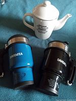 Teapot, blue travel mug, black travel mug grouped together
