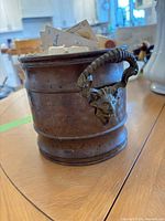 Side view of copper bucket with ram head handle filled with carded buttons