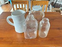 All four items on table: ceramic pitcher, two milk bottles, large jar with lid