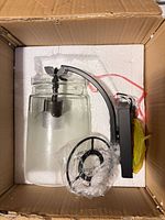 Wall sconce components in box: glass shade, metal arm/backplate, mounting ring and hardware