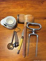 All items grouped on table: mallet, measuring cups, brass spoons, knife, honing steel, carving fork