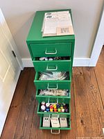Full view of green metal cabinet with multiple drawers partially open showing craft supplies