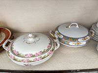 Two porcelain covered tureens side by side on shelf