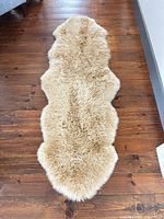 Full view of beige sheepskin runner rug on wooden floor
