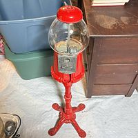 Full view of red pedestal gumball machine showing base, body, glass globe