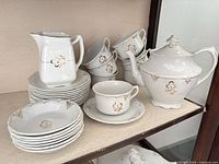 Teapot, creamer, stacked cups, saucers and small bowls displayed on shelf