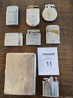 Eight silver-tone lighters and cigarette case laid out on table