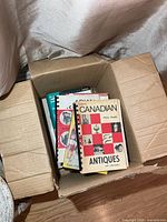 Box containing several collector reference books, top book Unitt's Canadian Antiques Price Guide visible