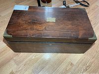 Closed writing box top showing wood grain, brass cartouche and corner guards