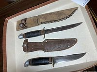 Two vintage knives with sheaths displayed in tray
