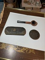Pipe, belt buckle and eyeglasses case grouped on board