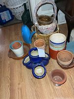 Assorted planters, wicker baskets and blue watering can grouped on floor