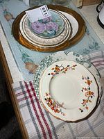 Stack of small raised-floral plates atop larger gold-rim plate alongside Alfred Meakin floral bowl