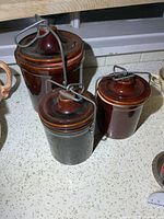 Three stoneware crocks grouped to show size comparison, lids and bails visible