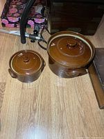 Both stoneware pots with lids side by side on floor