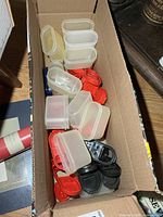 Box containing multiple translucent Tupperware spice containers with assorted lids